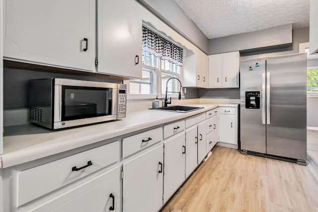 kitchen with appliances with stainless steel finishes, a sink, light wood-style flooring, light countertops, and a textured ceiling