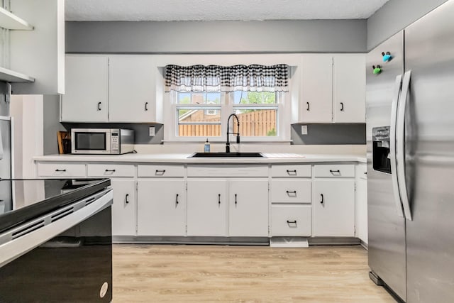 kitchen featuring appliances with stainless steel finishes, a sink, white cabinets, light wood-style flooring, and light countertops