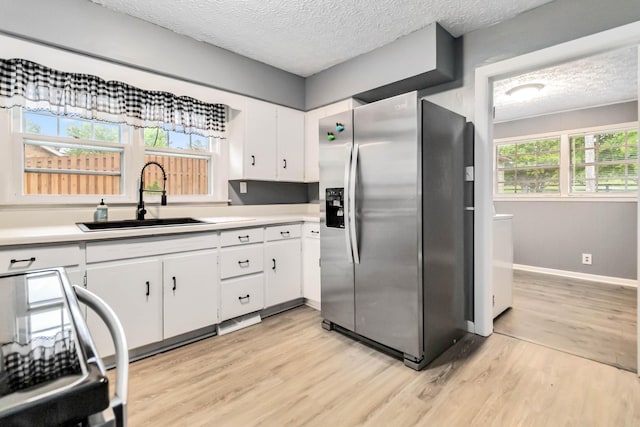 kitchen with stainless steel refrigerator with ice dispenser, a sink, light wood finished floors, a textured ceiling, and white cabinets