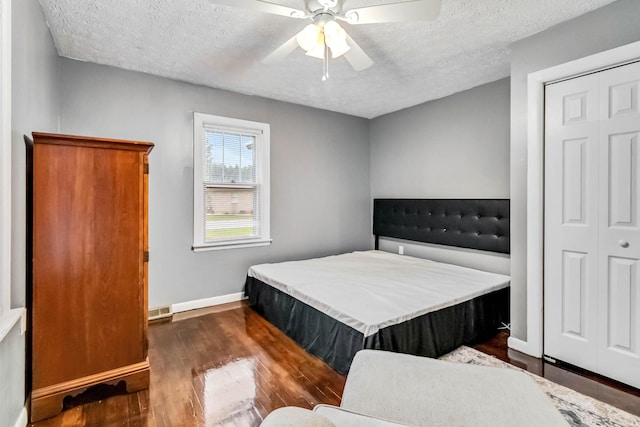 bedroom with dark wood-style floors, a textured ceiling, baseboards, a ceiling fan, and a closet
