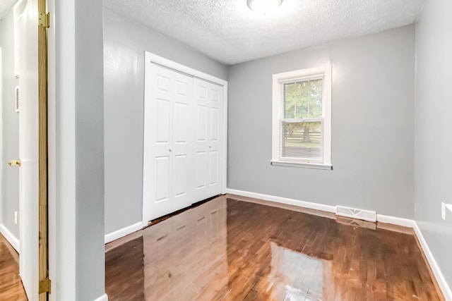 unfurnished bedroom with wood finished floors, baseboards, a closet, and a textured ceiling