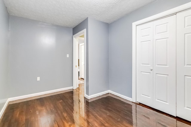 unfurnished bedroom featuring wood finished floors, a closet, baseboards, and a textured ceiling