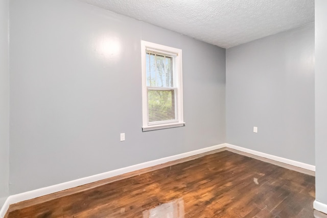 spare room featuring dark wood finished floors, a textured ceiling, and baseboards