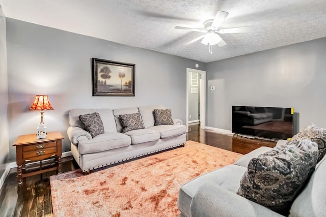living area featuring a ceiling fan, a textured ceiling, dark wood-style floors, and baseboards