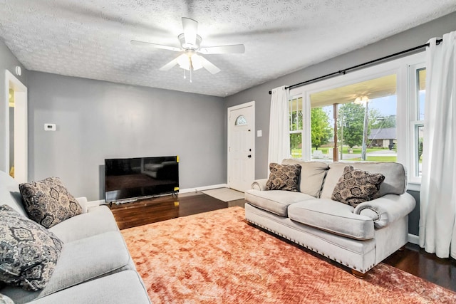 living area with dark wood-style flooring, a ceiling fan, a textured ceiling, and baseboards