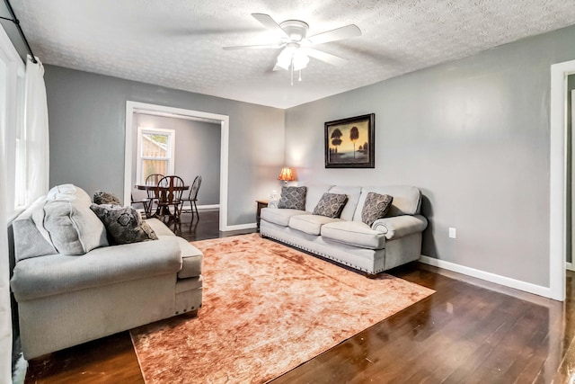 living room with ceiling fan, a textured ceiling, baseboards, and wood finished floors