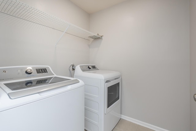 laundry area featuring washing machine and clothes dryer, light tile patterned floors, and baseboards