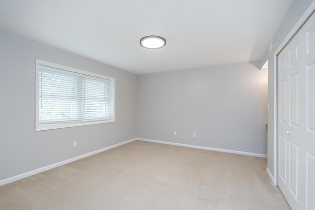 unfurnished bedroom with a closet, light carpet, and baseboards