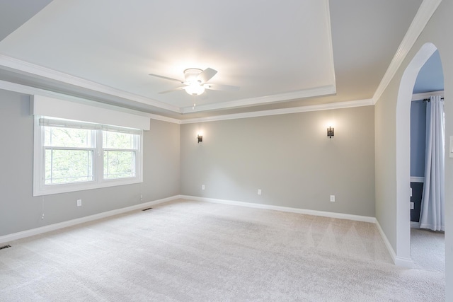 empty room with ornamental molding, a raised ceiling, light colored carpet, arched walkways, and ceiling fan