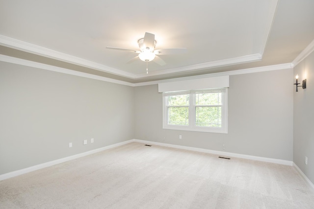 empty room with a tray ceiling, crown molding, a ceiling fan, baseboards, and light colored carpet