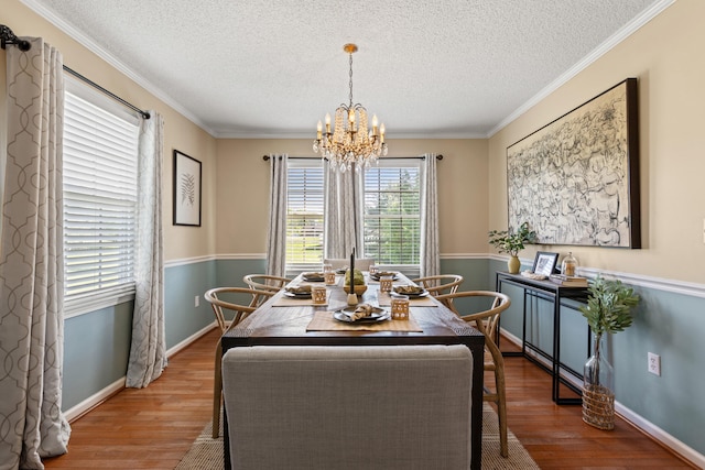 dining area featuring wood finished floors, a chandelier, a textured ceiling, ornamental molding, and baseboards