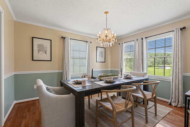 dining area featuring a chandelier, ornamental molding, a textured ceiling, wood finished floors, and baseboards