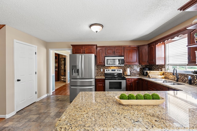 kitchen featuring stainless steel appliances, a sink, baseboards, backsplash, and dark stone finish floors