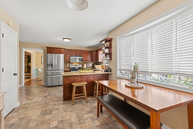 kitchen with stainless steel appliances, backsplash, stone finish flooring, a peninsula, and a textured ceiling