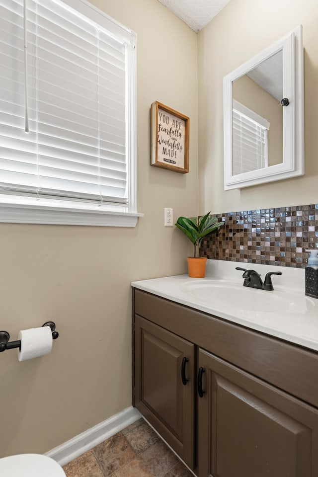 half bathroom featuring baseboards, vanity, and decorative backsplash