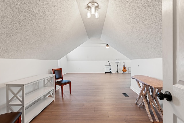 additional living space with a textured ceiling, lofted ceiling, baseboards, and wood finished floors