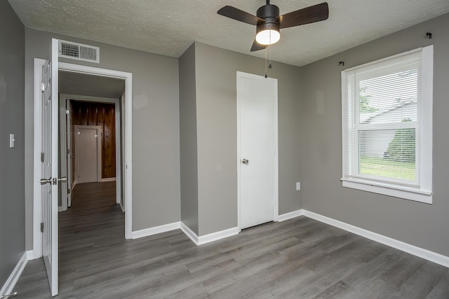 unfurnished bedroom featuring dark wood-style flooring, a textured ceiling, baseboards, and a ceiling fan