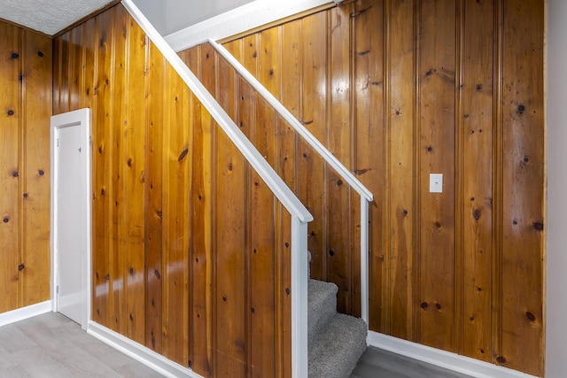 stairs with wood finished floors, baseboards, and wood walls