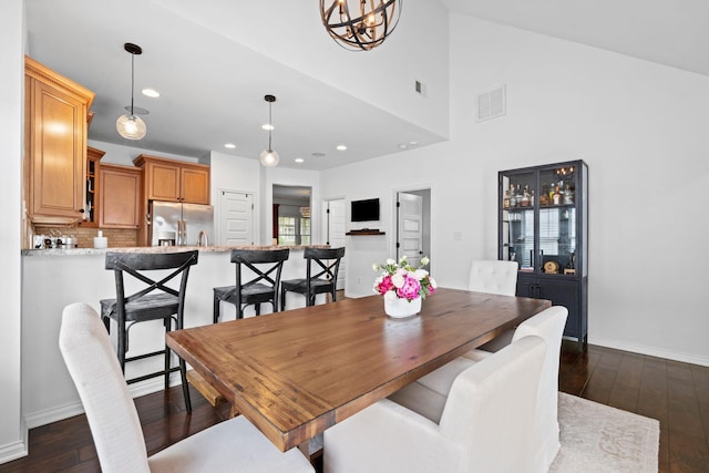 dining room featuring dark wood finished floors, recessed lighting, baseboards, a chandelier, and a high ceiling