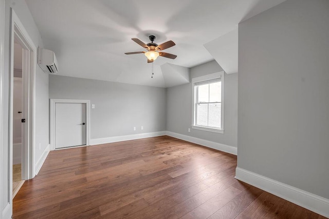 additional living space featuring a wall mounted air conditioner, ceiling fan, dark wood finished floors, and baseboards