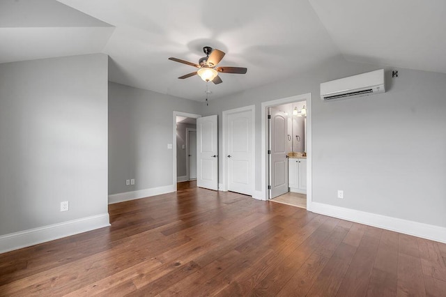 unfurnished bedroom with a wall mounted AC, lofted ceiling, wood finished floors, baseboards, and ensuite bath
