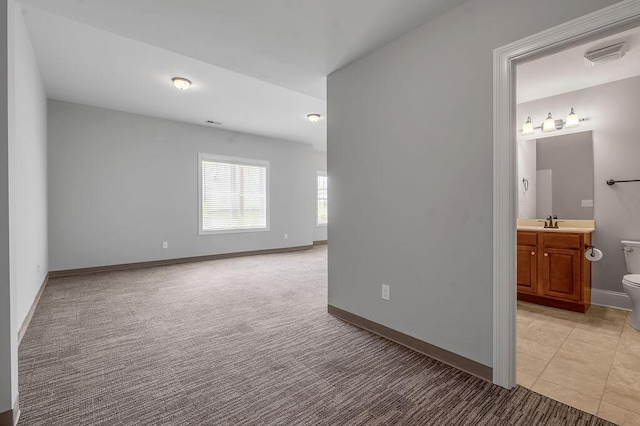 empty room featuring light colored carpet, baseboards, a sink, and light tile patterned floors