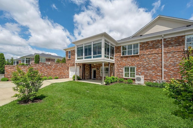 rear view of house with ac unit, concrete driveway, a sunroom, brick siding, and a yard