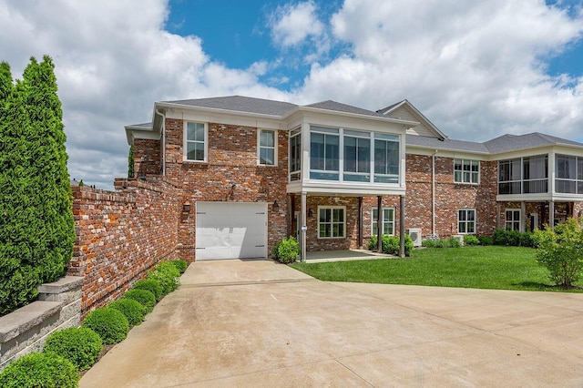 view of front facade with brick siding, concrete driveway, a sunroom, a garage, and a front yard