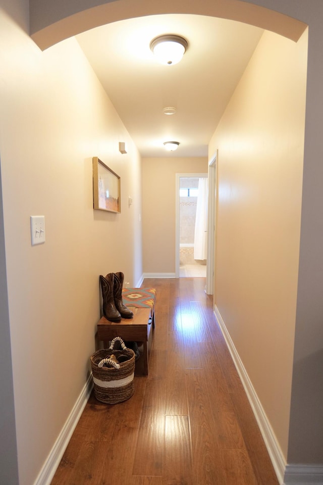 hall with wood-type flooring, arched walkways, and baseboards