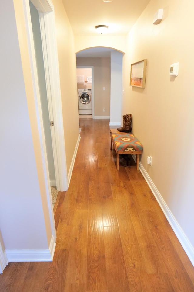 hall with washer / clothes dryer, arched walkways, light wood-style floors, and baseboards