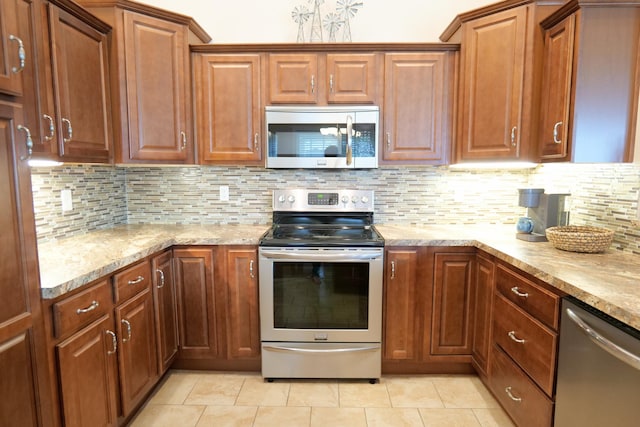 kitchen with appliances with stainless steel finishes, backsplash, light tile patterned floors, light stone counters, and brown cabinets