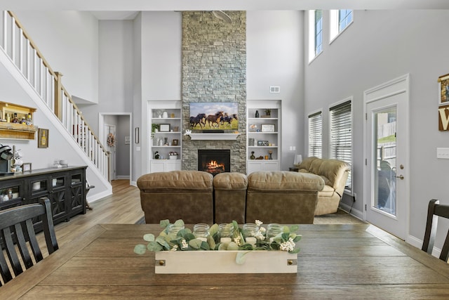 living room with a towering ceiling, stairway, light wood-style floors, a fireplace, and baseboards