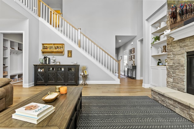 living area featuring a towering ceiling, wood finished floors, baseboards, stairway, and built in features