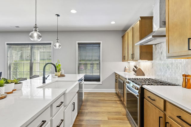 kitchen featuring appliances with stainless steel finishes, wall chimney range hood, a sink, light wood-type flooring, and light countertops