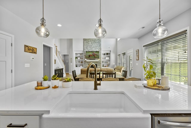 kitchen with a sink, built in shelves, open floor plan, a fireplace, and pendant lighting