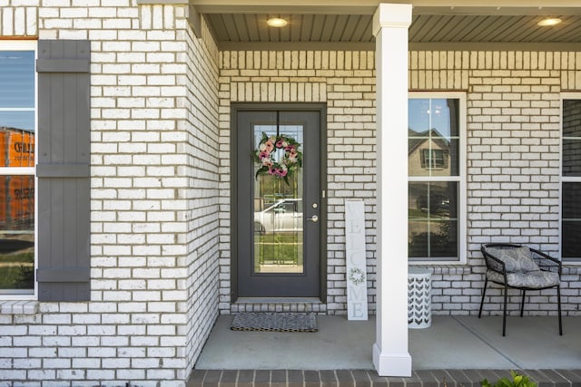 doorway to property with covered porch and brick siding