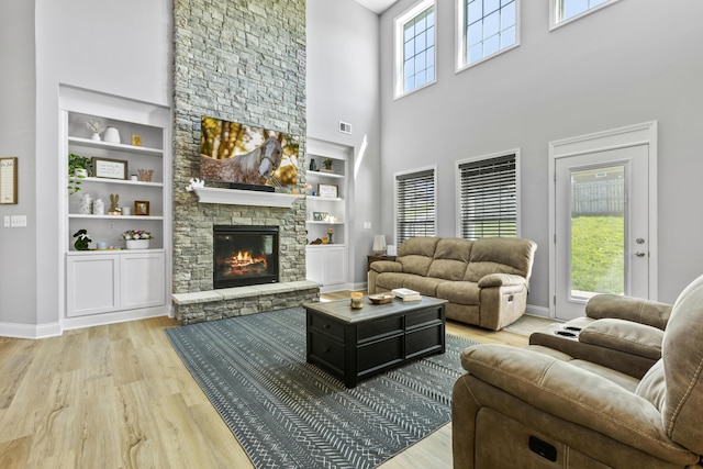living room with built in shelves, light wood-style floors, baseboards, and a high ceiling