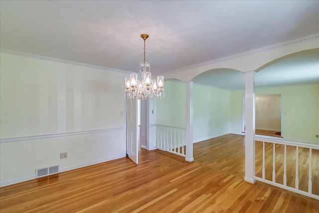 unfurnished dining area with arched walkways, a chandelier, ornamental molding, and wood finished floors