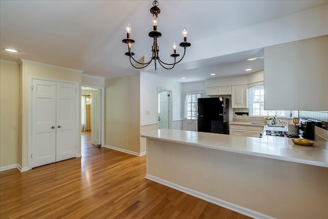 kitchen with freestanding refrigerator, light countertops, a chandelier, light wood finished floors, and a peninsula