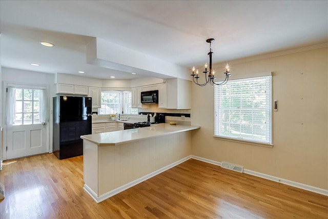kitchen featuring black appliances, a sink, a peninsula, a chandelier, and white cabinets