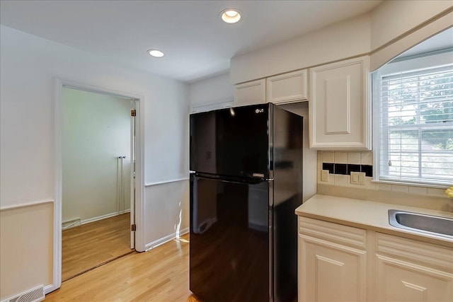kitchen with freestanding refrigerator, light wood-style flooring, a sink, light countertops, and white cabinets