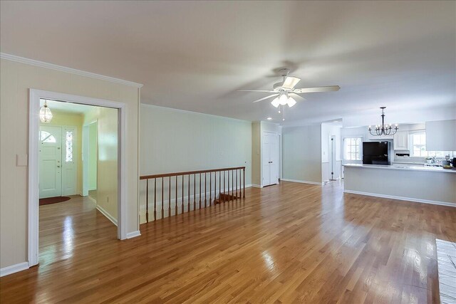 unfurnished living room with a chandelier, ceiling fan, light wood-style flooring, ornamental molding, and baseboards