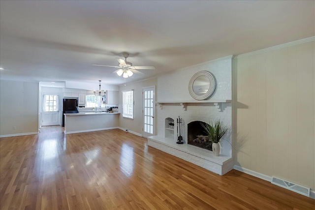 unfurnished living room with a chandelier, a fireplace, wood finished floors, healthy amount of natural light, and crown molding