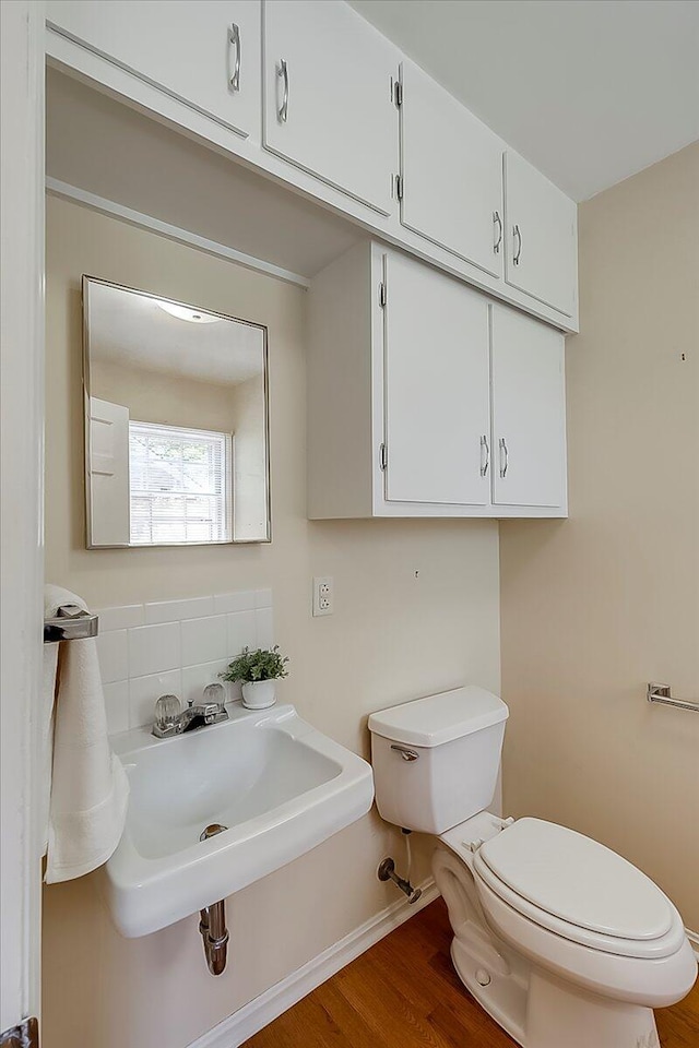bathroom featuring toilet, wood finished floors, decorative backsplash, a sink, and baseboards