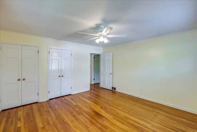 unfurnished bedroom featuring two closets, light wood-type flooring, baseboards, ornamental molding, and ceiling fan