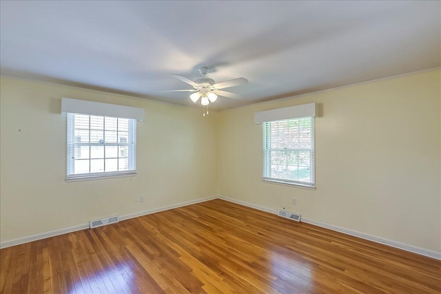empty room with plenty of natural light, wood-type flooring, a ceiling fan, baseboards, and ornamental molding