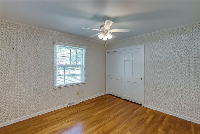 unfurnished bedroom with crown molding, light wood-style flooring, a closet, baseboards, and wallpapered walls