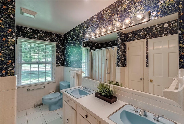 full bathroom featuring wallpapered walls, tile patterned flooring, wainscoting, tile walls, and toilet