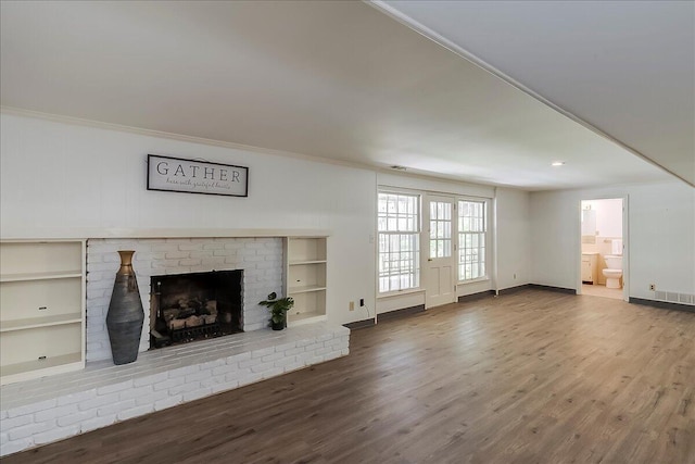unfurnished living room with wood finished floors, a fireplace, crown molding, and baseboards