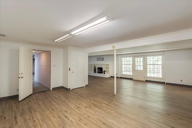 below grade area featuring light wood-style flooring, baseboards, and a fireplace with raised hearth